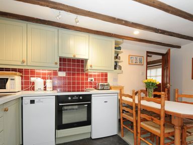 A kitchen with wooden beams red tiled backsplash appliances and a dining table with chairs and yellow flowers at The Granary Rock