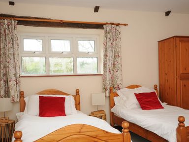 A bedroom with two wooden single beds with white bedding and red pillows a wooden wardrobe and floral curtains at The Granary in Rock