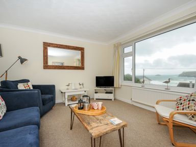 A living room with blue sofas a wooden coffee table a television and large window overlooking the sea at Trevega Polzeath
