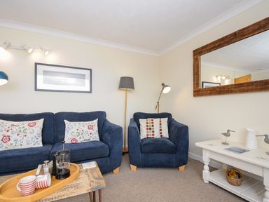 A living room with blue sofa and armchair a wooden coffee table and white side table with decorative items at Trevega Polzeath