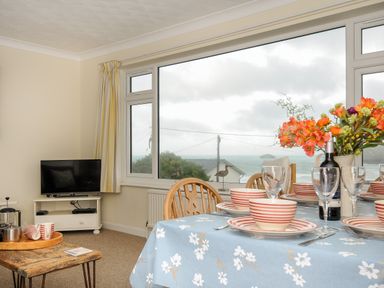 A dining area with a table set with plates bowls wine glasses and flowers next to a window with a sea view at Trevega in Polzeath