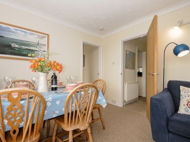 A dining area with a wooden table and chairs a blue tablecloth and a vase of flowers next to a blue sofa with a floor lamp at Trevega Polzeath
