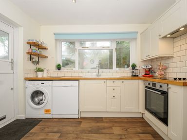 A kitchen with white cabinets wooden countertops washing machine dishwasher and oven at Trevega Polzeath