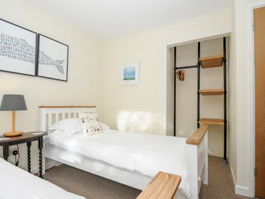 A bedroom with a single bed a side table with a lamp framed pictures and an open closet with shelves at Trevega in Polzeath