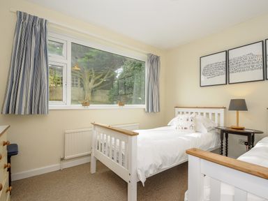 A bedroom with two single beds a bedside table with lamp and a large window with striped curtains at Trevega in Polzeath