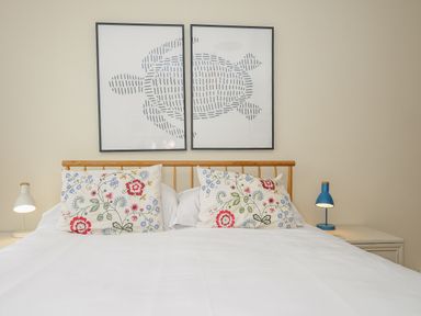 A bed with floral pillows and two framed turtle prints above at Trevega in Polzeath