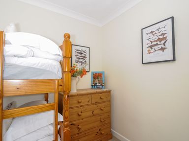 A bedroom corner with a wooden bunk bed a wooden dresser with flowers and a mirror and a framed shark poster on the wall at Trevega in Polzeath