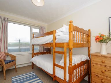 A bedroom with wooden bunk beds a wooden dresser with flowers a wicker chair and a window with striped curtains at Trevega Polzeath