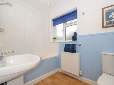 A bathroom with a white sink and bathtub blue towels and window blinds a radiator and a toilet at Trevega in Polzeath
