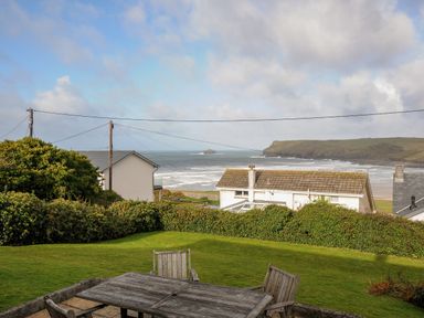 A backyard with wooden table and chairs overlooking houses hedge and ocean with cliff in the background at Trevega Polzeath