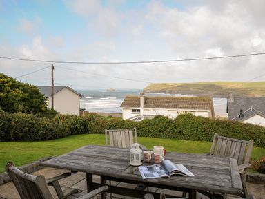 A wooden outdoor table with chairs on a patio overlooking houses bushes and the ocean at Trevega in Polzeath