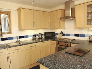 A kitchen with wooden cabinets a stove microwave kettle and sink at Polzeath Court 4 in Polzeath