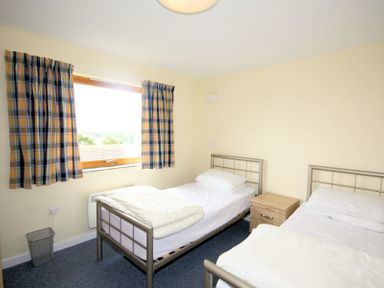 A bedroom with two single metal frame beds a wooden nightstand and a window with checkered curtains at Polzeath Court 4 Polzeath