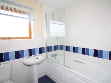 A bathroom with a bathtub a glass shower screen a pedestal sink a toilet and a window at Polzeath Court 4 in Polzeath