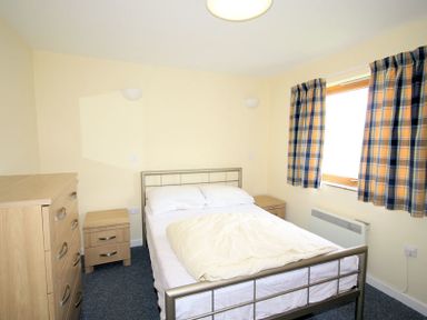 A bedroom with a metal bed frame dresser two bedside tables and a window with plaid curtains at Polzeath Court 4 in Polzeath