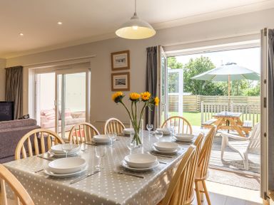 A dining room with a table set for eight people and sunflowers in a vase by open doors leading to a garden at Cogenhoe in Rock