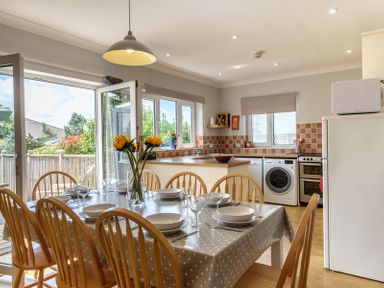 A kitchen and dining area with wooden chairs around a table set with dishes and glasses at Cogenhoe in Rock