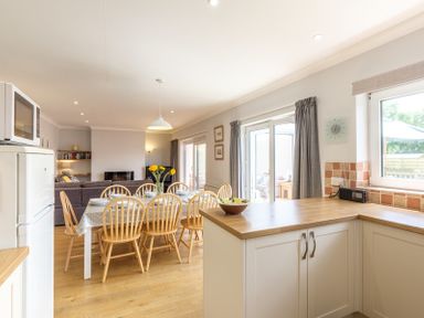 A kitchen and dining area with wooden chairs around a table set with plates and cups at Cogenhoe in Rock