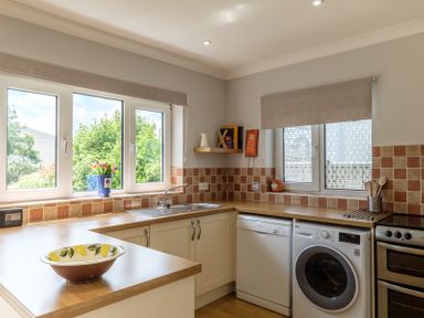 A kitchen with a washing machine dishwasher oven sink and windows with beige blinds at Cogenhoe in Rock