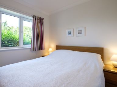 A bedroom with a double bed covered in a white bedspread two bedside tables with lamps a window with striped curtains and two framed pictures on the wall at Cogenhoe in Rock