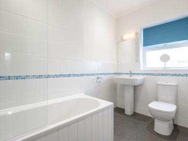 A bathroom with a bathtub a pedestal sink a toilet and a window with a blue blind at Cogenhoe in Rock
