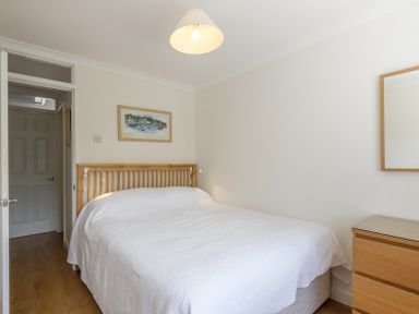 A bedroom with a double bed covered in a white bedspread wooden headboard a wooden dresser with a mirror and a framed picture on the wall at Cogenhoe in Rock