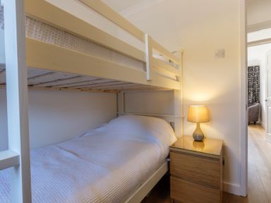 A bunk bed with a lower bed covered with white bedding and a wooden bedside table with a lamp in a bedroom at Cogenhoe in Rock