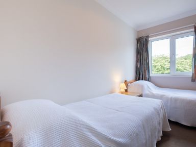 A bedroom with two single beds a nightstand with a lamp and a window with curtains at Cogenhoe in Rock