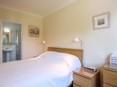 A bedroom with a bed a bedside table with a clock and a bathroom visible through an open door at Cogenhoe Rock