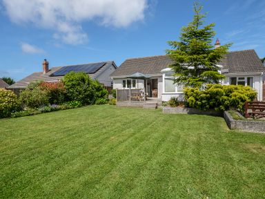 A backyard with a green lawn a tree shrubs and a white house with a small wooden deck and umbrella at Cogenhoe Rock