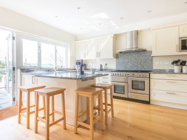 A kitchen with a central island and wooden stools and stainless steel appliances at Ragleighs in Daymer Bay