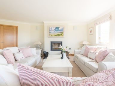 A living room with two white sofas and a white coffee table with flowers in a vase at Ragleighs in Daymer Bay