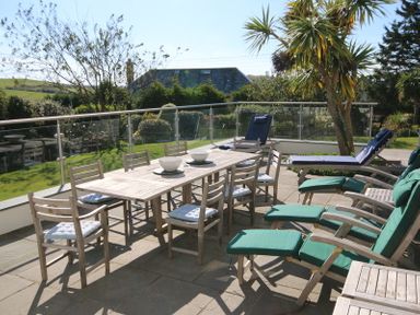 An outdoor patio with a wooden dining table and chairs with cushions and lounge chairs with green and blue cushions at Ragleighs in Daymer Bay