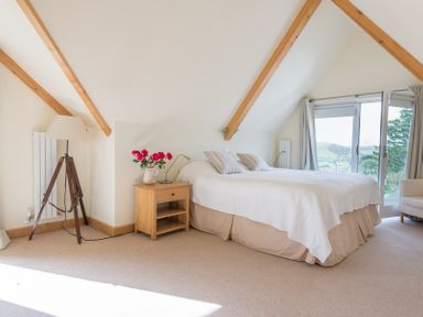 A bedroom with a bed pillows bedside table with flowers lamp and a door leading outside at Ragleighs in Daymer Bay