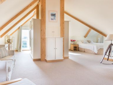 An attic bedroom with exposed wooden beams a bed sofa wardrobes bedside tables and lamps at Ragleighs in Daymer Bay