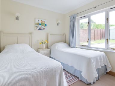 A bedroom with two single beds a nightstand with flowers and a window showing a fenced yard at Ragleighs Daymer Bay