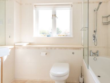 A bathroom with a toilet a bathtub with a shower and a window at Ragleighs in Daymer Bay