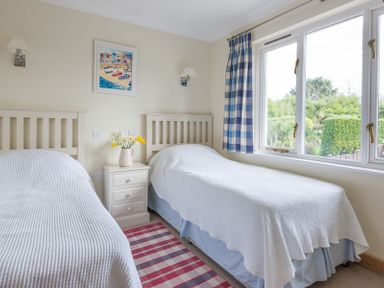 A bedroom with two single beds a bedside table with flowers and a window with blue plaid curtains at Ragleighs Daymer Bay