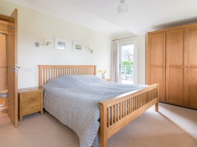 A bedroom with a wooden bed frame and grey bedspread two wooden nightstands wooden wardrobe and a door leading outside at Ragleighs in Daymer Bay