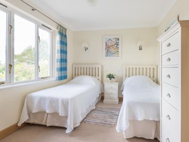 A bedroom with two single beds a bedside table a chest of drawers and a window with blue curtains at Ragleighs in Daymer Bay