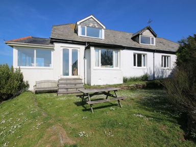 A white house with multiple windows and a wooden picnic table on a grassy lawn at Gullsway Kittiwake in Polzeath