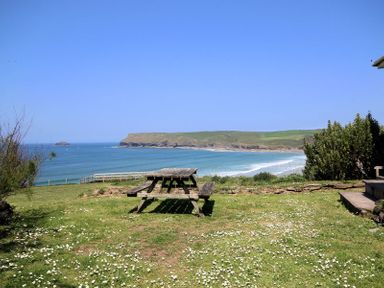 A picnic table on a grassy area overlooking a beach and cliffs at Gullsway Kittiwake Polzeath