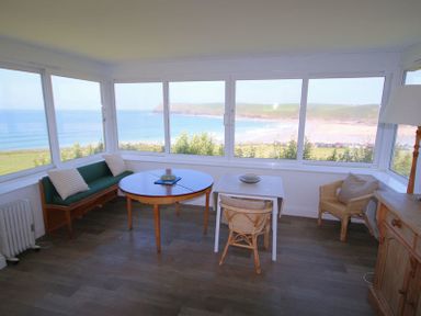 A room with multiple windows overlooking the sea with tables chairs and a wooden sideboard at Gullsway Kittiwake in Polzeath