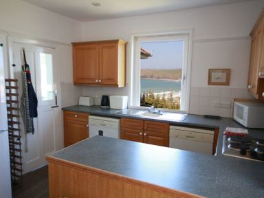 A kitchen with wooden cabinets, dishwasher, microwave, and a window overlooking the sea at Gullsway Kittiwake Polzeath
