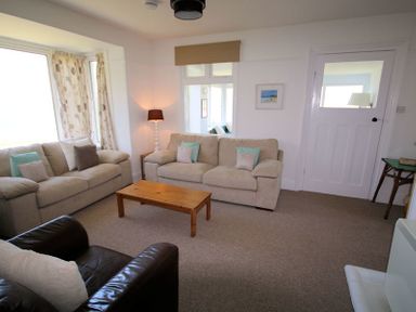 A living room with two beige sofas a dark armchair a wooden coffee table and a floor lamp at Gullsway Kittiwake Polzeath