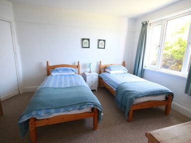 A bedroom with two single beds a nightstand and a lamp by a window at Gullsway Kittiwake Polzeath