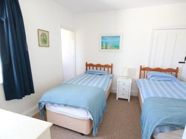 A bedroom with two single beds with blue striped bedding a white nightstand and blue curtains at Gullsway Kittiwake in Polzeath