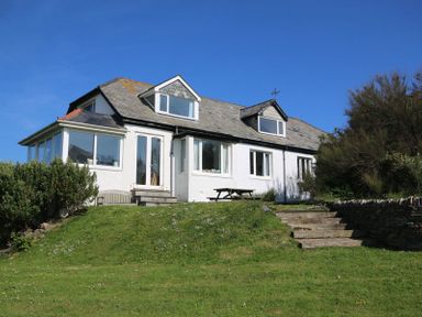 A white house with a slate roof surrounded by grass and bushes at Gullsway Sandpiper Polzeath