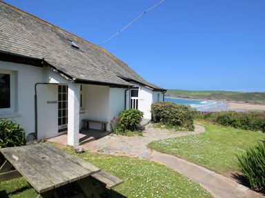 An exterior view of a white house with a slate roof a picnic table on grass and a beach in the background at Gullsway Sandpiper Polzeath
