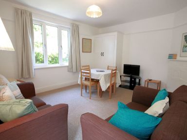 A living room with brown sofas and teal cushions a dining table with chairs and a small television in the corner at Gullsway Sandpiper Polzeath
